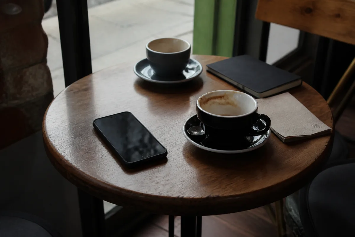 Téléphone posé sur une table de café après un premier rendez-vous, avec un carnet et deux tasses dans une ambiance naturelle