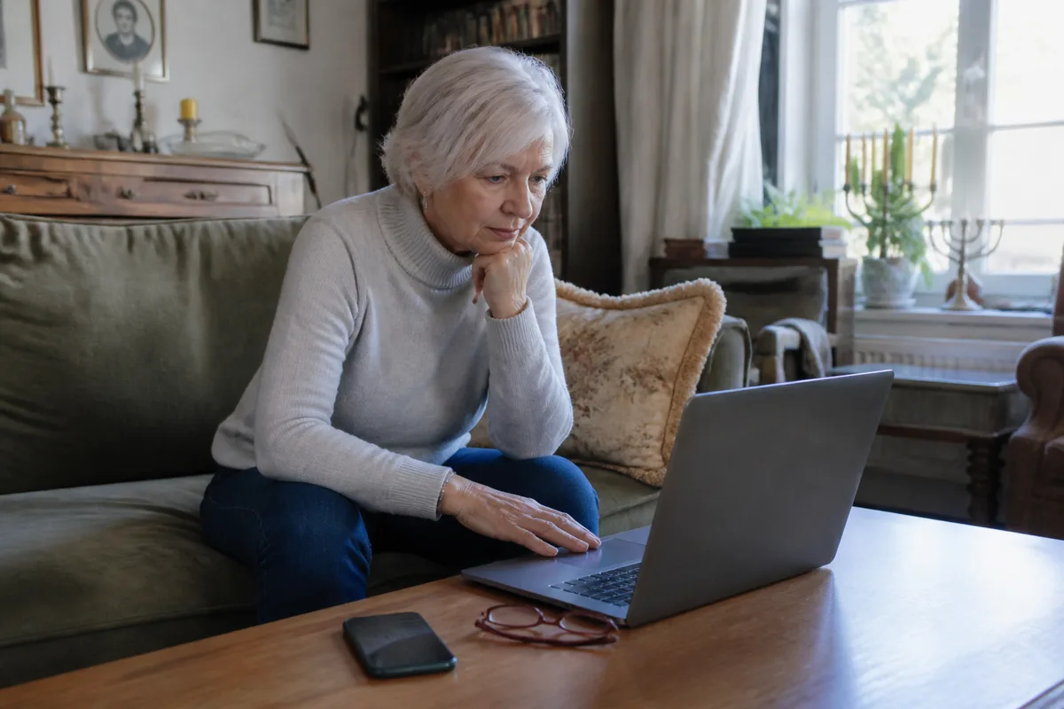 Personne de plus de 60 ans utilisant un site de rencontre gratuit dans un salon lumineux, avec téléphone posé à côté